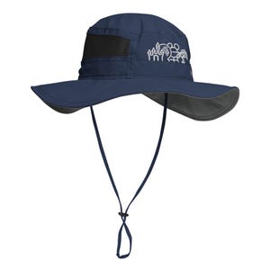 May include: A navy blue sun hat featuring a wide brim, a black mesh ventilation panel, and a chin strap with an adjustable toggle. The side of the hat displays a white line art graphic of a castle, a circular icon, and a tree silhouette.