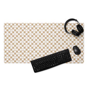 May include: A rectangular desk mat with a brown and white checkered pattern featuring Mickey Mouse silhouettes. A black keyboard, mouse, and headphones are on the mat.