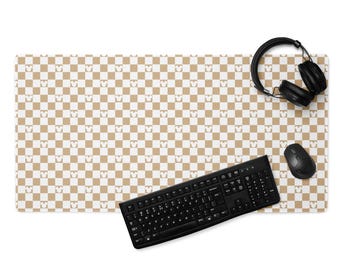 May include: A rectangular desk mat with a brown and white checkered pattern featuring Mickey Mouse silhouettes. A black keyboard, mouse, and headphones are on the mat.