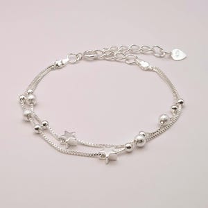May include: A silver chain bracelet with two strands, featuring small round beads and star charms.