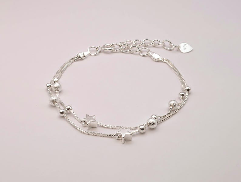 May include: A silver chain bracelet with two strands, featuring small round beads and star charms.