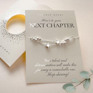 May include: A silver bracelet with star and bead accents is displayed on a card that reads "Here's to your NEXT CHAPTER." The card also includes the text "Your talent and determination will make this journey a remarkable one. Keep shining!"