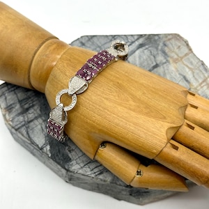 May include: A silver bracelet with a chain link design and pink gemstones. The bracelet is adorned with small, round, clear gemstones.