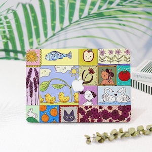 May include: A rectangular laptop hard shell case featuring a colorful grid of hand-drawn illustrations including a fish, apple, flowers, wheat, ducks, a dog, a tomato, swans, a rabbit, oranges, and a cat, with a central cutout for an Apple logo.