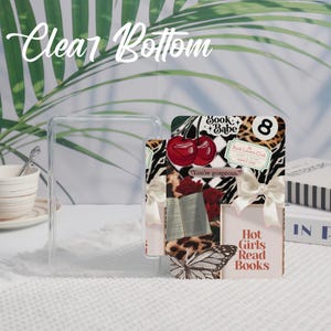 May include: A clear, rectangular phone case with the text "Clear Bottom" in a cursive font. A decorative card features cherries, a butterfly, and the text "Hot Girls Read Books". The card has a zebra print and a leopard print.