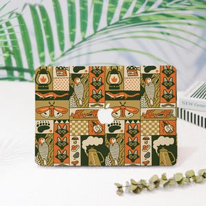 May include: A laptop skin featuring a repeating grid pattern of nature-themed illustrations in orange, dark green, and cream. The design includes lanterns, moths, foxes, birds, bears, beetles, mushrooms, and coffee pots with a central Apple logo cutout.