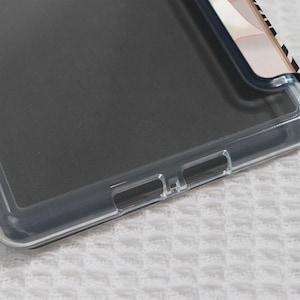 May include: A clear phone case with a black interior. The case has a transparent border and cutouts for buttons and ports. The top right corner features a design with black and white stripes and pink accents.