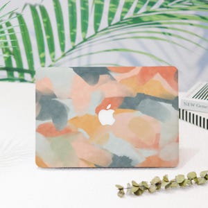 May include: A laptop computer with a colorful abstract design on the cover. The design features a mix of pink, orange, yellow, and blue watercolor-like shapes. The Apple logo is visible on the cover.