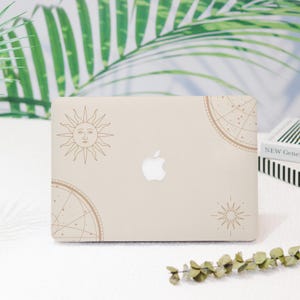 May include: A beige laptop computer with a gold sun, compass, and star design. The laptop has a white Apple logo.