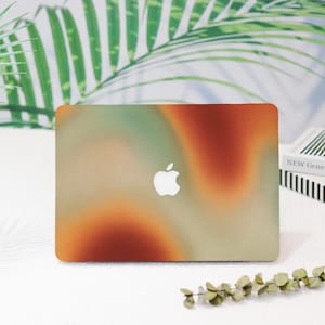 May include: A laptop computer with a colorful abstract design on the cover. The design features shades of orange, green, and brown. The Apple logo is visible on the cover.