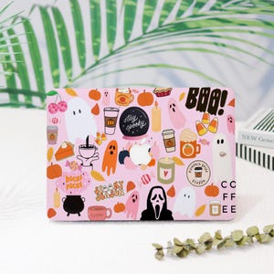 May include: Pink laptop skin with a variety of Halloween and fall themed stickers. The stickers include ghosts, pumpkins, candy corn, coffee cups, and the text "Boo!" and "Stay Spooky".