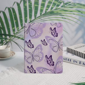 May include: A notebook with a butterfly design. The cover features a pattern of purple butterflies on a light purple and white background. The butterflies vary in size and are outlined in dark purple.