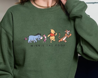 May include: A green sweatshirt with a Winnie the Pooh graphic featuring Winnie the Pooh, Piglet, Eeyore, and Tigger walking in a line. The text "Winnie the Pooh" is printed below the graphic.