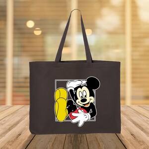 Puede incluir: Un bolso tote marr&oacute;n oscuro con una imagen de dibujos animados de Mickey Mouse en un marco cuadrado blanco. Mickey Mouse se representa en una pose relajada, con guantes blancos, zapatos amarillos y una camisa roja. El bolso tiene asas largas.