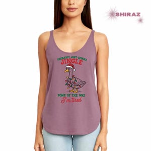May include: Mauve tank top featuring a cartoon goose wearing a Santa hat and Christmas lights. Text reads "Probably just gonna Jingle some of the way I'm tired". The tank top has a scoop neck and a curved hemline.