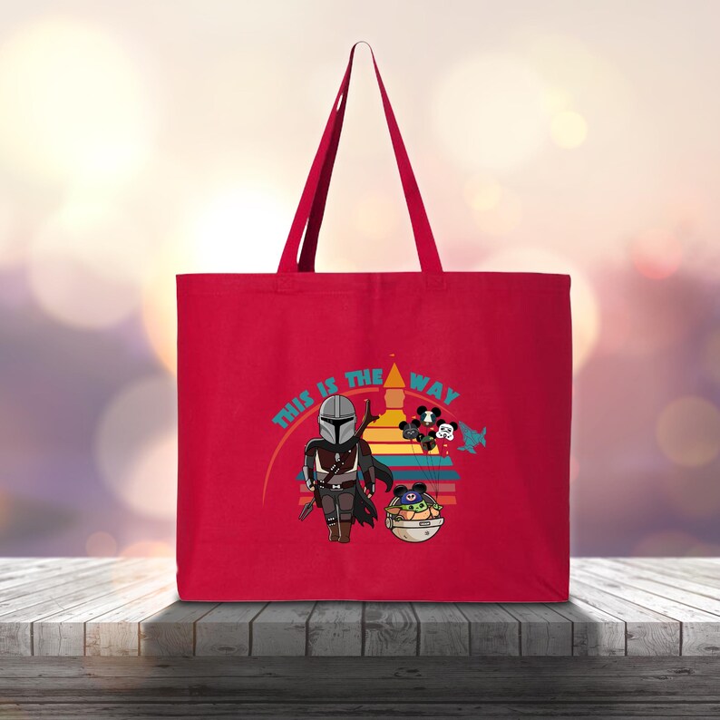 May include: Red tote bag with a cartoon illustration of The Mandalorian, Grogu, and Mickey Mouse characters. The phrase "This is the Way" is printed above the characters in a colourful design. The bag has long handles.