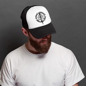 May include: A black and white trucker hat with a mesh back. The hat features a black and white graphic of a tree with a sword through it.