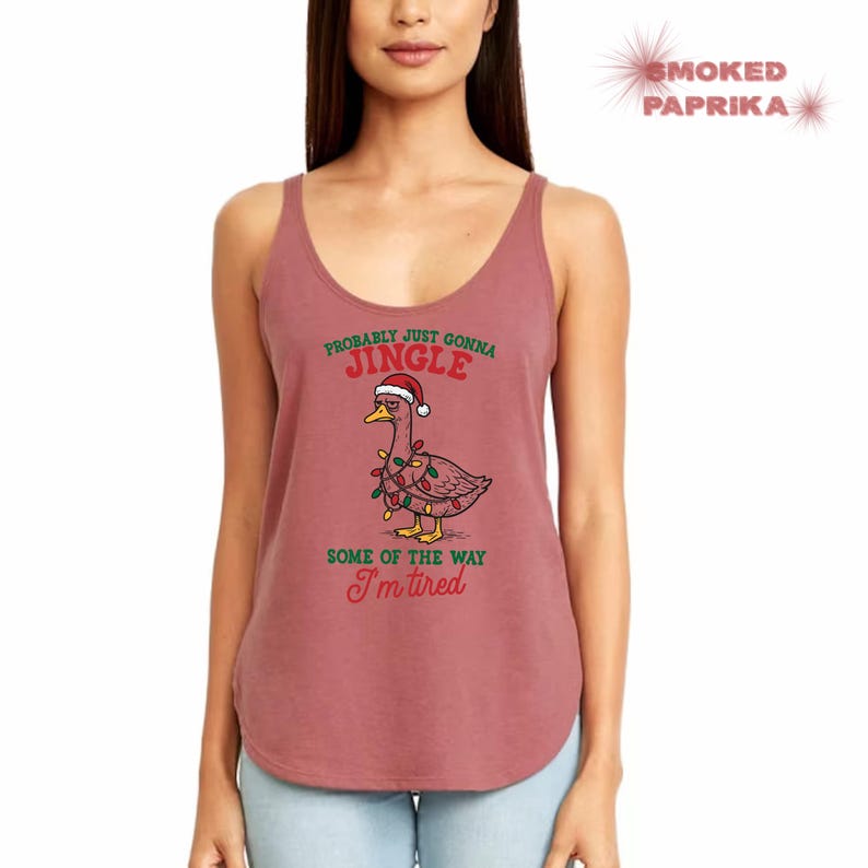 May include: A dusty rose tank top with a humorous Christmas graphic. The graphic features a cartoon goose wearing a Santa hat and string lights, with the text "Probably just gonna jingle some of the way I'm tired."