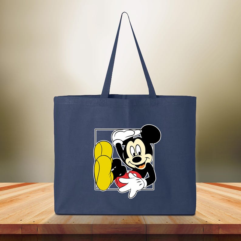Puede incluir: Bolso tote azul marino con un gr&aacute;fico de Mickey Mouse en un cuadrado blanco. El personaje de dibujos animados es de color negro, blanco, rojo y amarillo. El bolso tiene dos asas azul marino. Adecuado para llevar objetos.