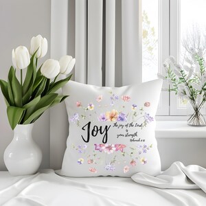 May include: A white decorative pillow with a floral design and the word "Joy" in black script. The pillow features a watercolor-style arrangement of pastel-colored flowers and the text "The joy of the Lord is your strength. Nehemiah 8:10."