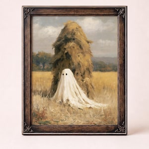 Puede incluir: Una lámina de arte enmarcada que muestra la pintura de una figura fantasmagórica blanca con dos ojos negros circulares de pie en un campo de trigo dorado frente a un gran pajar. La obra está dentro de un marco decorativo de madera marrón.