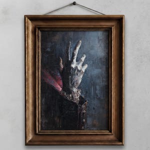 May include: An oil painting in a gold-toned wooden frame depicts a pale hand reaching upwards against a dark, textured background. The hand is the focal point, with visible details and a dramatic pose. A red fabric is visible.