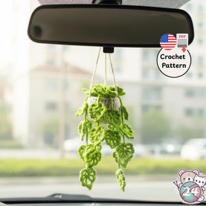 May include: A handmade crochet hanging plant, featuring a light green leafy design cascading from a gray pot. The plant hangs from a string, suspended from a car's rearview mirror. The image includes a "Crochet Pattern" graphic.