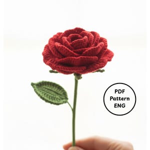 May include: A handcrafted red crochet rose with green stem and leaf. The rose is in full bloom, showcasing detailed petal work. The stem is held by a hand. A circular graphic with "PDF Pattern ENG" is in the image.