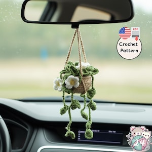 May include: A crocheted hanging plant decoration with a woven basket, green leaves, and white flowers. The plant hangs from a beige string and is suspended from a car's rearview mirror. The image includes a "Crochet Pattern" graphic.