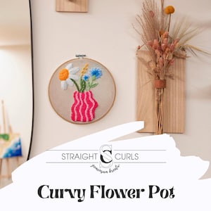 Może przedstawiać: Okrągły, haftowany obraz na ścianę przedstawiający wazon w różowo-białe paski, z białymi stokrotkami, niebieskimi kwiatami i zielonymi łodygami. Pod haftem znajduje się napis "Curvy Flower Pot". Widoczna jest również nazwa marki "Straight Curls".