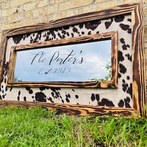 Pu&ograve; includere: Specchio rettangolare con cornice in legno rustico e bruciato. Lo specchio &egrave; circondato da un motivo a pelle di mucca. Il testo "The Porter's Est. 2013" &egrave; scritto sullo specchio in corsivo.