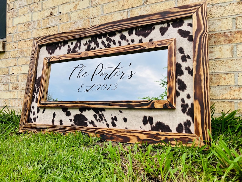 Pu&ograve; includere: Specchio rettangolare con cornice in legno rustico e bruciato. Lo specchio &egrave; circondato da un motivo a pelle di mucca. Il testo "The Porter's Est. 2013" &egrave; scritto sullo specchio in corsivo.