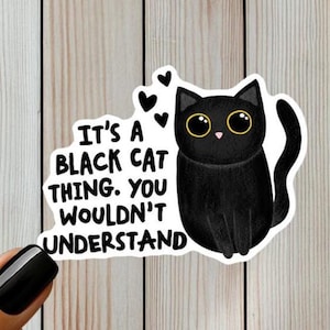 Op de afbeelding: Een gestanste sticker met een zwarte kat met grote gele ogen en een omhoog gekrulde staart. Boven de kat staan drie kleine zwarte hartjes. De tekst luidt: It's a black cat thing. You wouldn't understand. De sticker heeft een witte rand.
