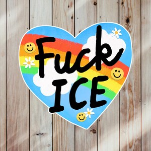 Puede incluir: Una pegatina en forma de coraz&oacute;n con fondo azul, un arco&iacute;ris y las palabras "Fuck ICE" en negro. El dise&ntilde;o incluye nubes blancas, margaritas y caras sonrientes.