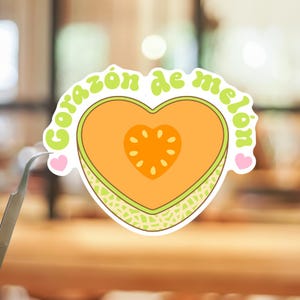 May include: A die-cut sticker featuring a heart-shaped cantaloupe melon with a light green rind and orange flesh. The center contains a heart-shaped seed cavity. The text Corazón de melón is arched above in light green, with two small pink hearts.