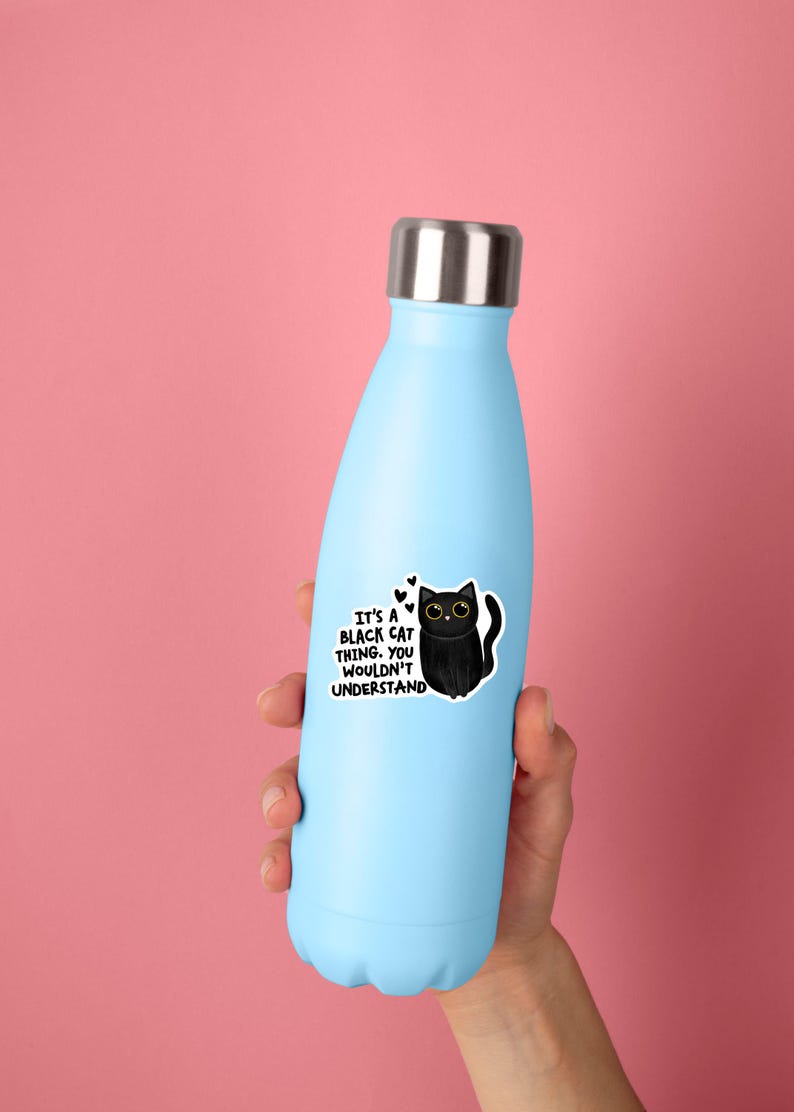 Op de afbeelding: Een lichtblauwe waterfles met een zilverkleurige metalen dop. Een sticker op de fles toont een zwarte cartoonkat met grote gele ogen en de tekst: IT'S A BLACK CAT THING. YOU WOULDN'T UNDERSTAND, vergezeld door drie kleine zwarte hartjes.