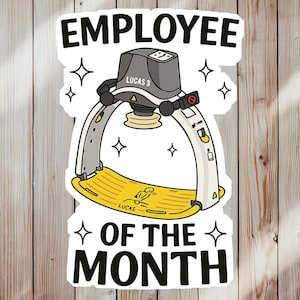 May include: A sticker with the text "EMPLOYEE OF THE MONTH" in black, featuring a cartoon illustration of a medical device. The device is gray and white with a yellow base, and the name "LUCAS 3" is visible.