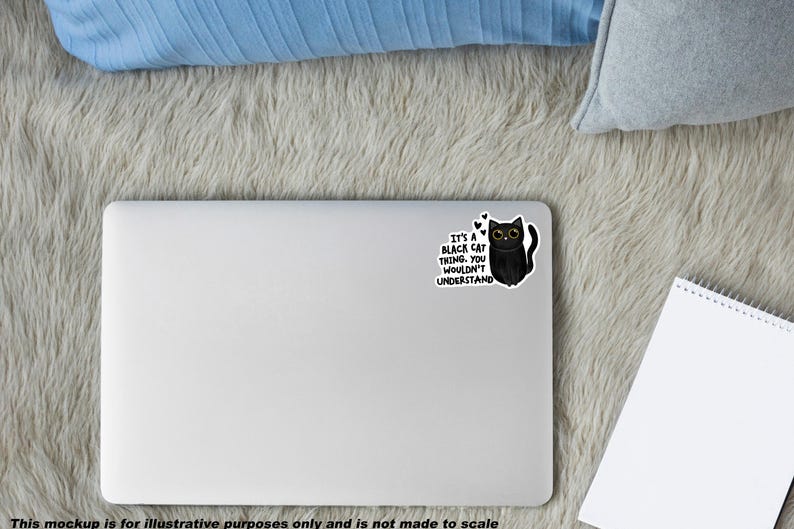 Op de afbeelding: Een zilveren laptop met een sticker van een zwarte kat met grote ogen en de tekst: It's a black cat thing. You wouldn't understand. De sticker bevat kleine hartjes boven de kat, die in een cartoonstijl is afgebeeld op de laptop.