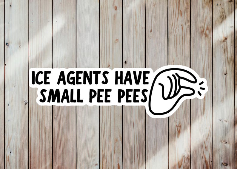 May include: A white sticker with black text that reads "ICE AGENTS HAVE SMALL PEE PEES" and a black and white graphic of a hand gesture. The sticker is on a light brown wooden surface.