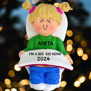 May include: A personalized Christmas ornament featuring a girl sitting on a toilet with the text "I'm a big kid now! 2024" and the name "Anita".