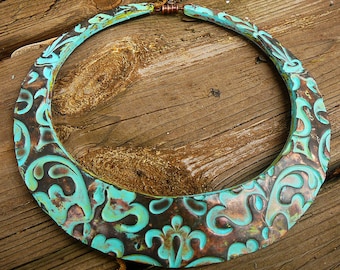 May include: A turquoise and copper necklace with a decorative, embossed pattern. The necklace is made of metal and has a rounded, crescent shape.