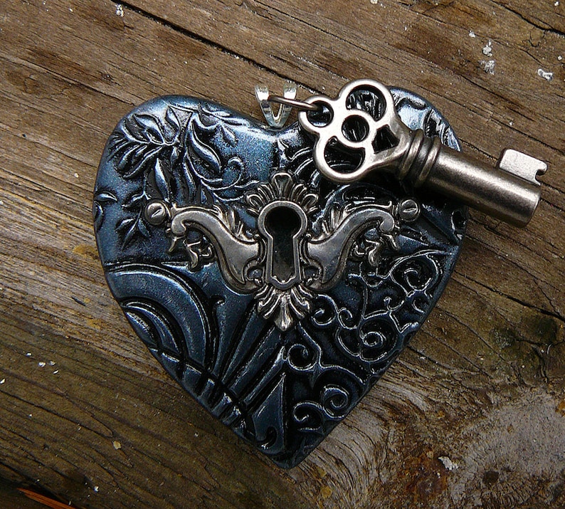 May include: A dark blue heart-shaped pendant with an intricate design and a keyhole. A silver key with a decorative head is attached to the pendant.
