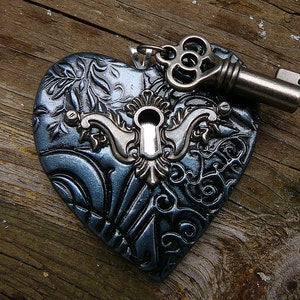 May include: A dark blue heart-shaped pendant with a silver keyhole and a silver key attached. The heart has a detailed, ornate design.
