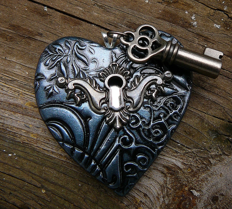 May include: A dark blue heart-shaped pendant with a silver keyhole and a silver key attached. The heart has a detailed, ornate design.
