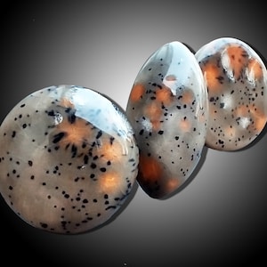 May include: Three smooth, oval-shaped stones with a mottled pattern of black, white, and orange. The stones are polished and have a glossy finish.
