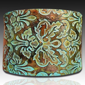 May include: A copper cuff bracelet with a turquoise blue and brown embossed floral pattern.