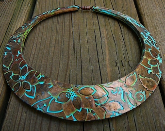 May include: A large, copper-colored necklace with a turquoise floral design. The necklace is made of metal and has a rounded shape.