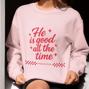 May include: A light pink sweatshirt with the text "He is good all the time" in red script. The text is accompanied by red starbursts. Below the text is "PSALM 100:5" in white text.