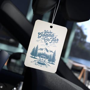 May include: A white car air freshener with a blue and white illustration of a van driving through a mountain landscape. The text "You're Gonna Go Far" is written in blue cursive lettering.