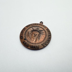 May include: A copper-colored commemorative medallion featuring the Statue of Liberty. The medallion is circular with the text "STATUE OF LIBERTY CENTENNIAL 1886-1986" around the edge. The Statue of Liberty's face is in the center.